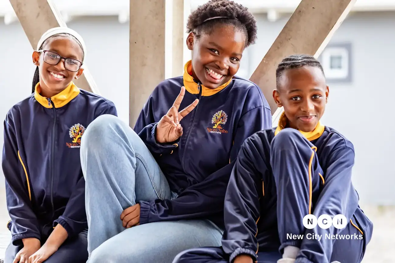 Three Nguzo Saba learners in full school uniform, sitting together and smiling